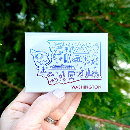 Hand holding a card with a stylized illustration of Washington state against a green leafy background