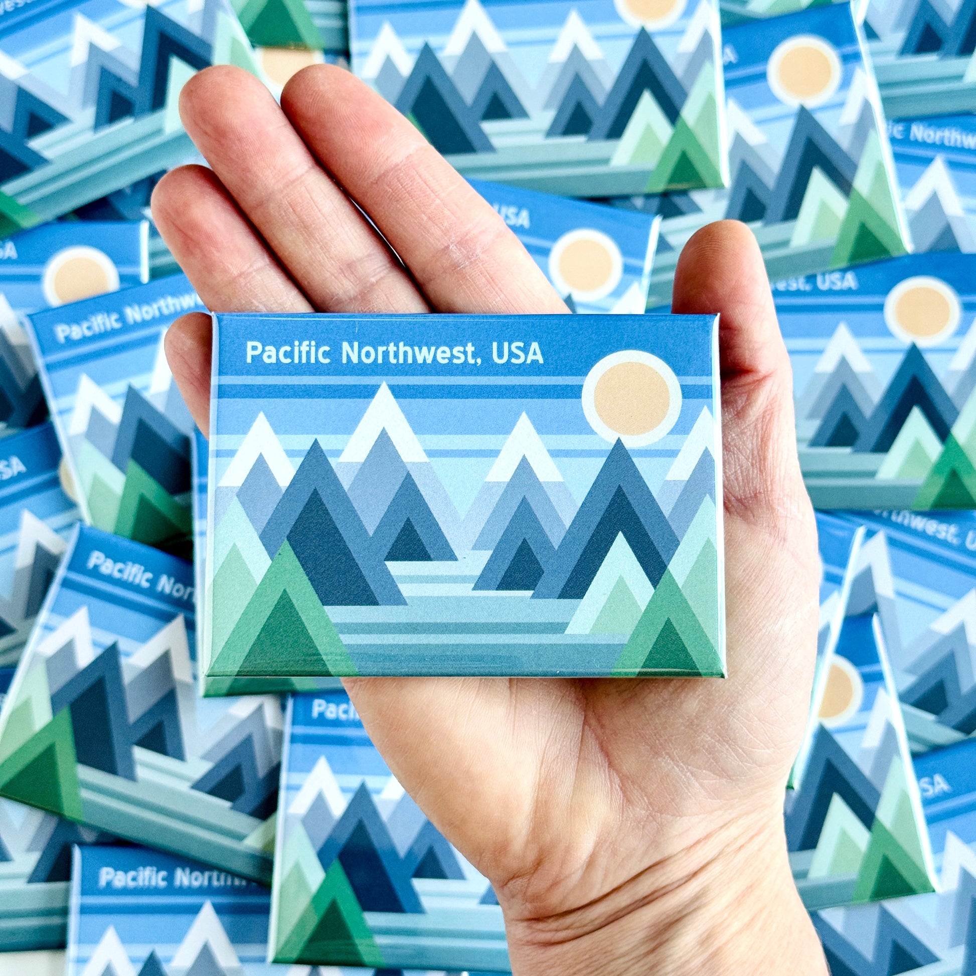 Hand holding a Pacific Northwest-themed magnet with more magnets in the background