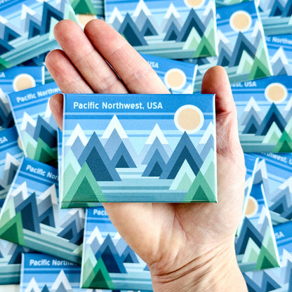 Hand holding a Pacific Northwest-themed magnet with more magnets in the background