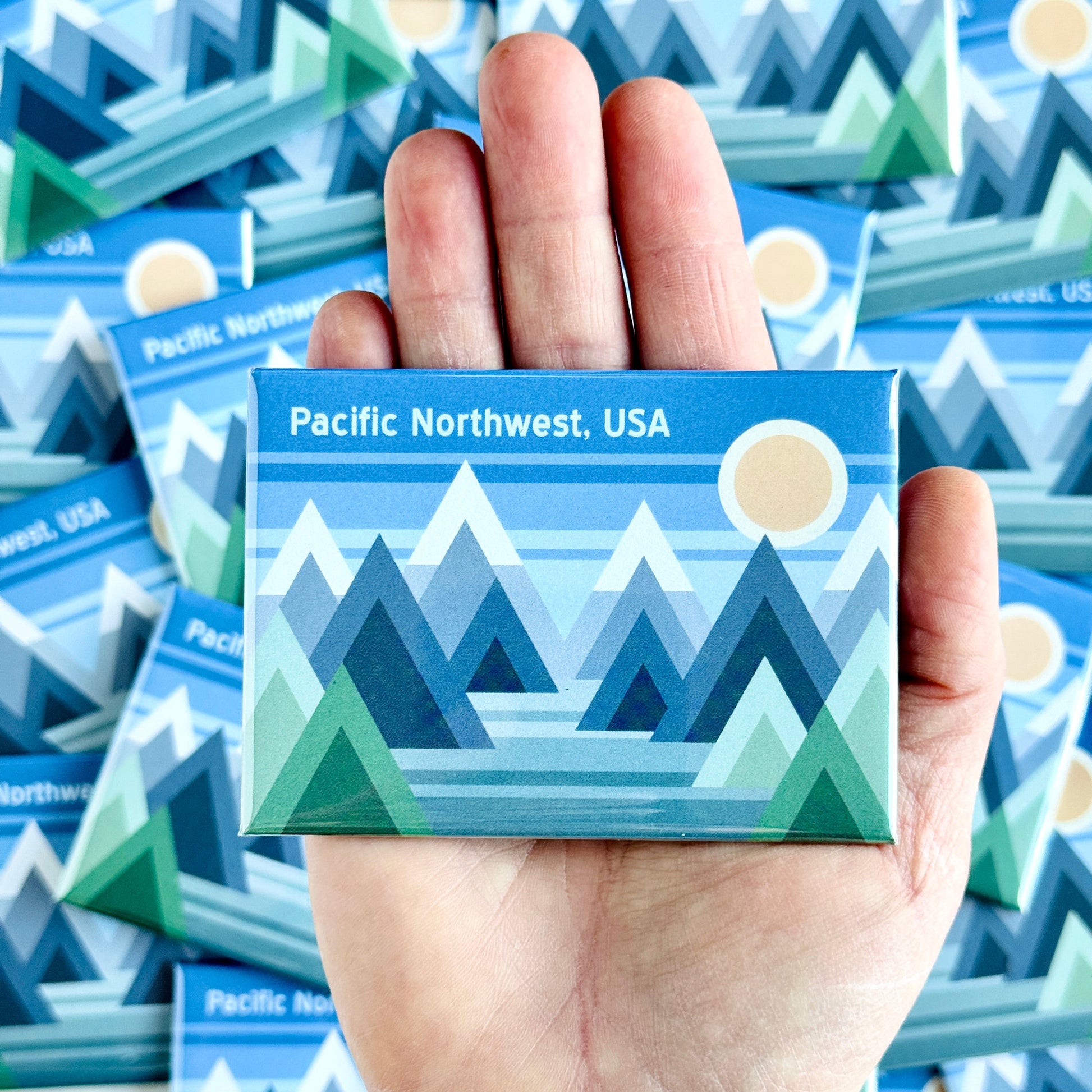 Hand holding a Pacific Northwest USA magnet with more magnets in the background.